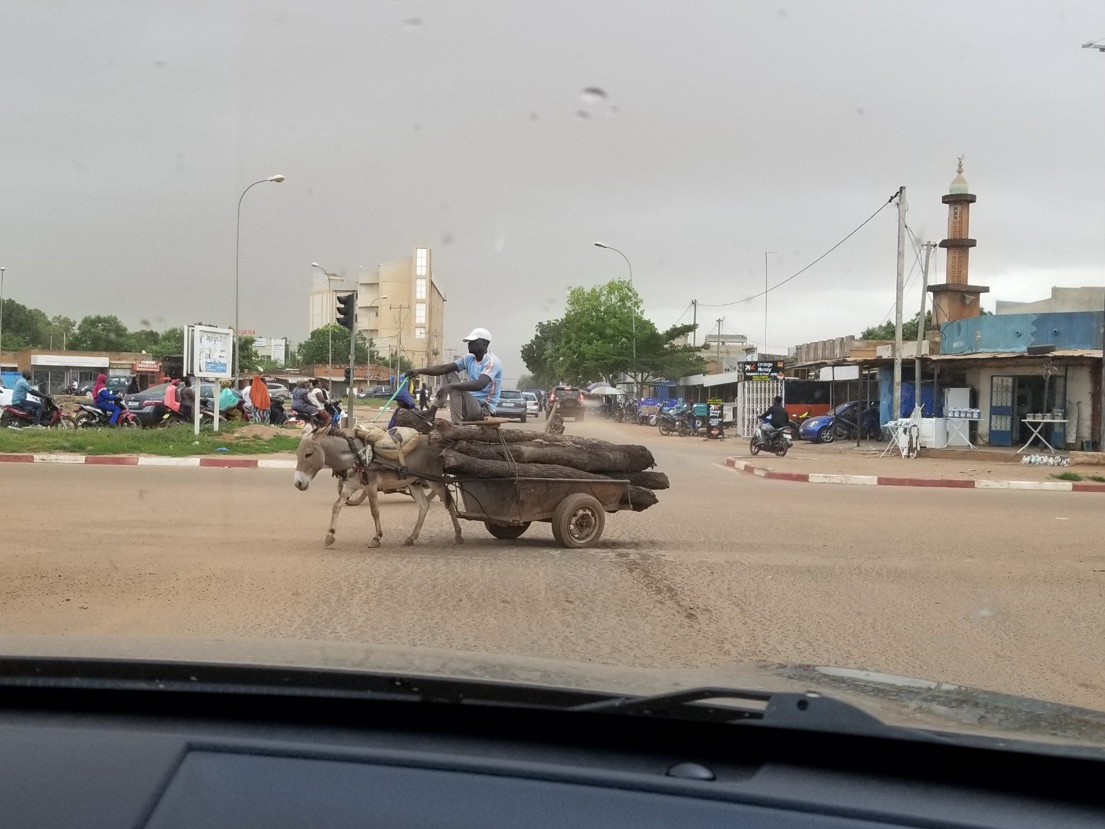 A man drives a donkey cart loaded with firewood through a busy city intersection in Ouagadougou, Burkina Faso, with a mosque and shops in the background